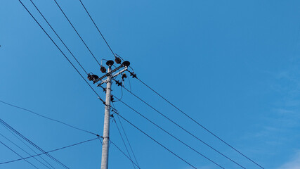 Electric utility pole with power lines crossing a clear blue sky. Urban electricity infrastructure, energy distribution cables, minimal outdoor scene, technology and connection concept