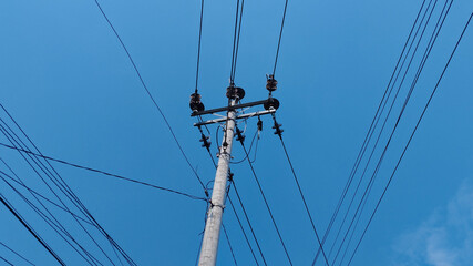 Fototapeta premium Electric utility pole with power lines crossing a clear blue sky. Urban electricity infrastructure, energy distribution cables, minimal outdoor scene, technology and connection concept