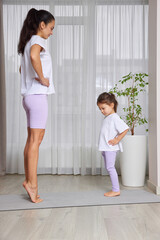 Mother and daughter standing on yoga mat, doing workout at home
