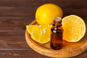 Lemon essential oil in a bottle with sliced ​​lemon and leaves on a wooden background. Lemon oil. Perfume bottle with aromatic essential oil. Serum, lemon extract. Vitamin C. Natural cosmetics. 