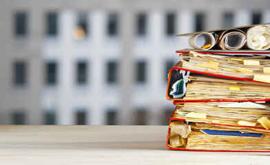 Messy file folders, ring binders grungy paperwork.Red tape, bureaucracy, overworked, beat the clock business concept on blurred office building background.