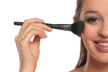 Studio shot of a smiling woman’s half face applying blush with a makeup brush on a white background