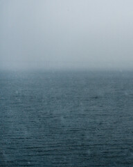 A minimalist seascape on an overcast day: an endless expanse of water with fine ripples, gradually fading into thick fog on the horizon. Cool blue and gray tones create an atmosphere of tranquility, m