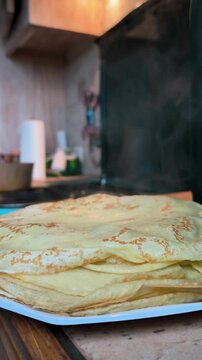 Beautifully stacked golden crepes on a white plate in a kitchen.