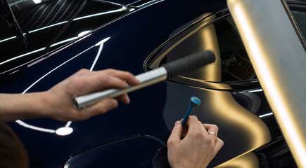 Process of paintless dent repair on car body. The mechanic at the auto shop with tools to repair dents in car body. Body repair. A specialist repairs a dent on the car body without painting. PDR. 