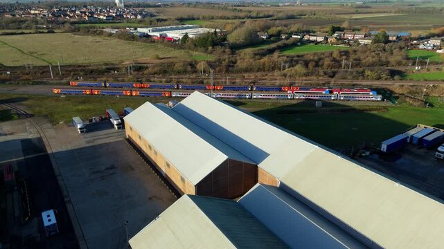 Aerial view of trains parked beside large buildings, offering a stark contrast between industrial elements and the rural backdrop, Ely, England, United Kingdom.