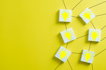 Network of square blocks with yellow light bulb icons connected by lines on yellow background....