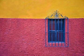Colonial house facade with a pink and ochre textured wall and a window with blue handcrafted iron...