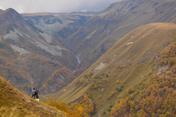 Couple Standing On Steep Cliff Edge Overlooking Autumn Mountain Canyon