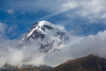 Mount Kazbek Snow Capped Peak In Clouds Against Blue Sky
