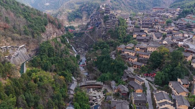 Aerial view of Wangxian Valley's traditional buildings nestled amidst lush greenery and rugged terrain, creating a striking contrast, Wangxian Valley, China.