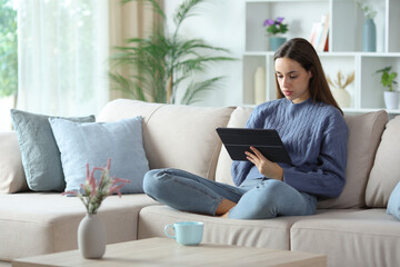 Serious woman in blue using digital tablet on a sofa