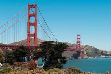 Golden Gate Bridge connecting Marin Headlands and San Francisco Peninsula, standing tall against a clear blue sky, with surrounding hills and the bay below creating a beautiful scenic vista