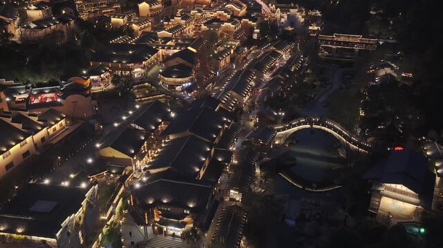 Aerial view of Wangxian Valley at Night showing the illuminated buildings and bridge reflecting light on the water, Wangxian, China.