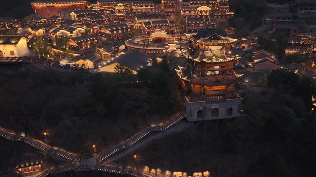 Aerial view of illuminated traditional buildings and pathways in Wangxian Valley, creating a warm glow against the night, Wangxian Valley, China.