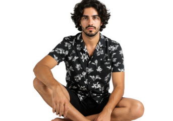 Man with curly hair wearing a floral shirt sitting cross legged isolated on transparent background