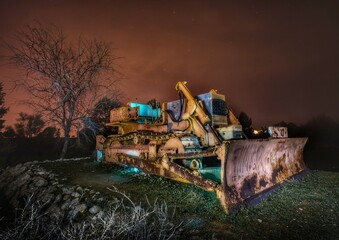 A vintage or antique bulldozer in an old barn under the light of a lantern.