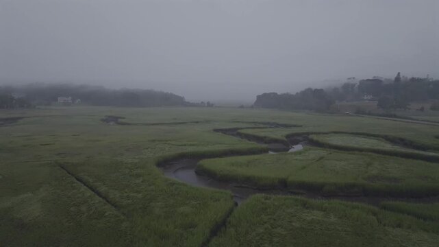 Aerial view of winding river cutting through a marshy landscape under a heavy, gray sky, a scene of muted tones and serene stillness, Gloucester, Massachusetts, United States.