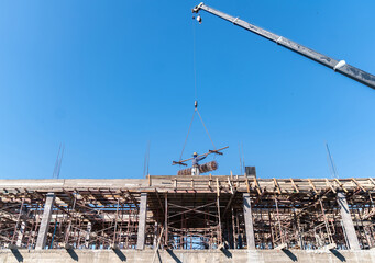 Mobile crane lifting steel reinforcement rebar to a worker on top of a building structure.