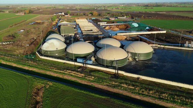Aerial view of a Biogas Plant, its dome-shaped digesters contrasting with the adjacent green fields, creating a juxtaposition of technology and nature, Wisbech, United Kingdom.
