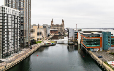 Aerial view of Princes Dock waterfront with modern architecture and the historic Royal Liver Building in Liverpool, England, under an overcast sky.