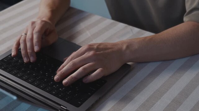 Close up shot from a slight side and top angle showing male hands typing on a laptop keyboard. Camera captures natural wrist position, steady finger movement and calm everyday computer work. 4k
