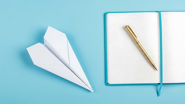 White Paper Airplane and Gold Pen on Blue Notebook Against Light Blue Background