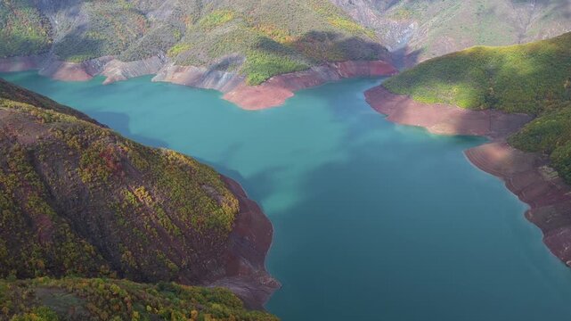 Aerial video of Fierza Lake with emerald water surrounded by autumn-colored hills and rugged shorelines in northern Albania.