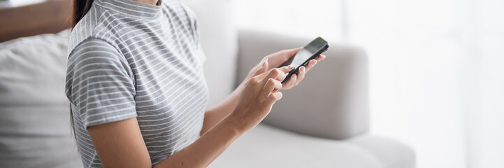 Asian Woman controlling smart home. mobile phone with smart home app in living room. touch screen...