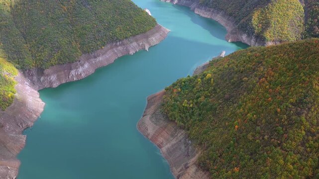 Aerial video of Fierza Lake with emerald water surrounded by autumn-colored hills and rugged shorelines in northern Albania.