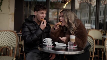 A young couple is enjoying a romantic date at a in Paris France They are sharing a croissant and coffee while sitting at an outdoor table The scene captures a lifestyle love and travel concept in a Pa