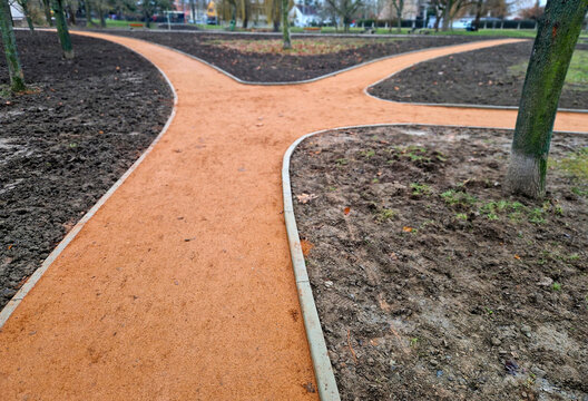 newly constructed or renovated park pathway. Path self-binding gravel path decomposed granite orange beige color, which contrasts well with surroundings.​Edging path is clearly defined by concrete cur