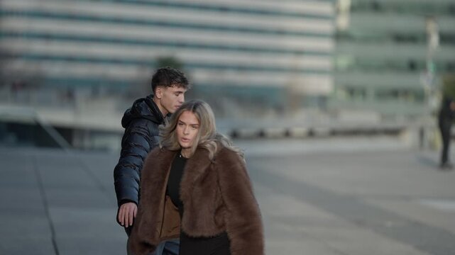 A young couple is arguing on a city street in Paris France The man and woman appear to be in disagreement with modern architecture visible in the background The scene suggests relationship problems or