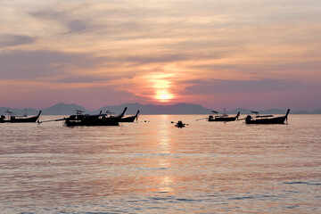 Obraz premium Several boats drift gently as sunset turns the sky and water shades of lavender and orange, creating a tranquil moment on the open sea. Krabi, Thailand.