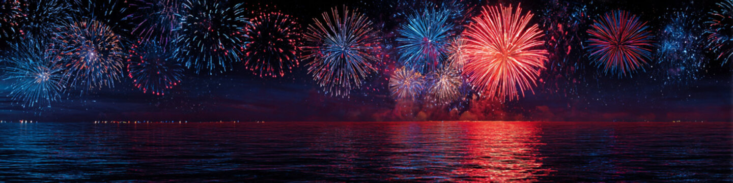 A stunning nighttime display of colorful fireworks exploding above a serene body of water with vibrant reflections on the surface