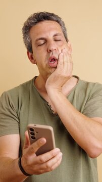 Worried man with gray hair using his mobile phone, showing a range of negative emotions from shock and disbelief to frustration and anger. Vertical