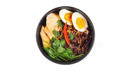Top view of spicy chicken ramen with boiled eggs, spinach, mushrooms, and chili pepper in a black...