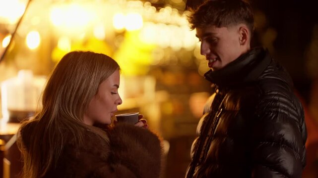 A romantic couple in Paris France at night The woman is holding a coffee cup and the man is smiling Bokeh lights are visible in the background The scene depicts winter love romance and travel.