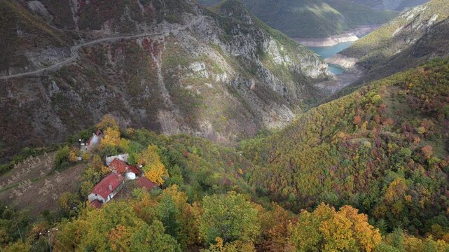 Aerial video of a winding mountain road above Fierza Lake, with dramatic cliffs, forested slopes, and alpine peaks in the distance.