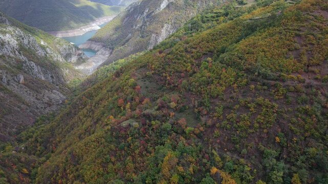 Aerial video above Fierza Lake, with dramatic cliffs, forested slopes, and alpine peaks in the distance.