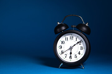 Naklejka premium Black alarm clock on blue background with copy space.