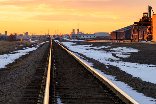 Railroad tracks run through an industrial area at sunset in Amarillo, Texas. Warehouses and industrial buildings line the rail corridor as warm light reflects off the rails. 