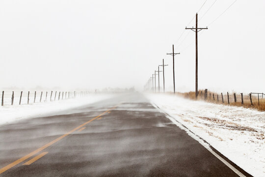 A rural road disappears into blowing snow in the Texas Panhandle near Amarillo. Power lines and fences frame the scene, emphasizing winter weather and isolation. 