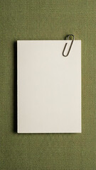 A blank white notepad with a paperclip on a green textured background, ready for notes.
