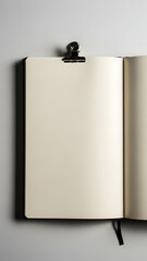 An open notebook with blank cream-colored pages held by a black binder clip, featuring a bookmark ribbon.