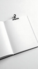 Open blank notebook with white pages and a metal clip on a clean white background.