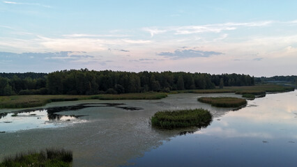 Fototapeta premium A serene view of a wide river surrounded by lush greenery under a pastel sky at dusk. Reflections on the water create a tranquil atmosphere, perfect for nature and tourism themes.