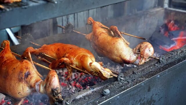 Whole ducks roasting on rotating spits over charcoal grill at street food stall
