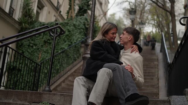 A young couple sits on the steps in Montmartre Paris France The lovers are embracing on the stairs with ivy-covered railings The outdoor scene captures a moment of affection and togetherness in the ci