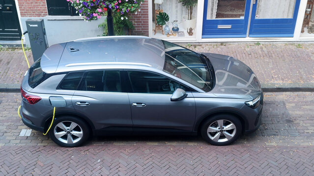 High-angle side view of a modern grey electric SUV charging at a public station on a brick-paved street in the Netherlands. Concept of green energy and urban EV infrastructure.
